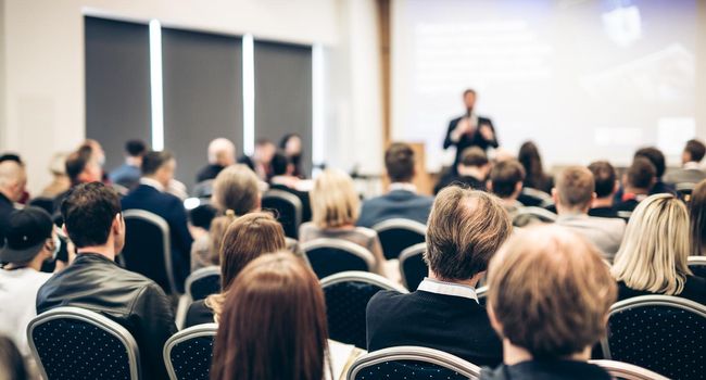 Speaker giving a talk in conference hall at business event. Rear view of unrecognizable people in audience at the conference hall. Business and entrepreneurship concept