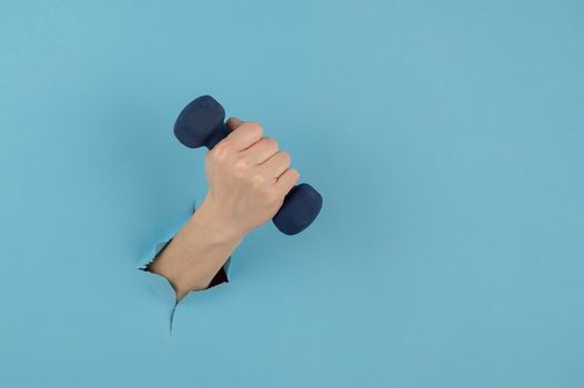 A female hand sticking out of a hole from a blue background holds a dumbbell