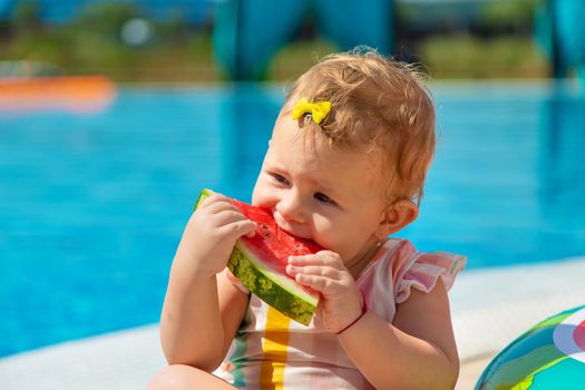 Baby is eating a watermelon by the pool. Selective focus. Kids.