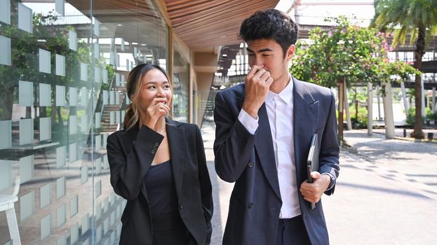 Two happy business colleagues having a discussion while walking outside modern office building.