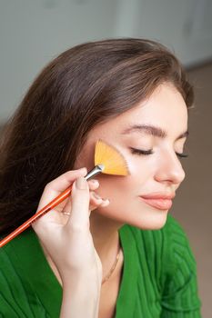 Make up artist applying professional make up of tonal foundation on the face of beautiful young caucasian woman in make up room. Base for make up.