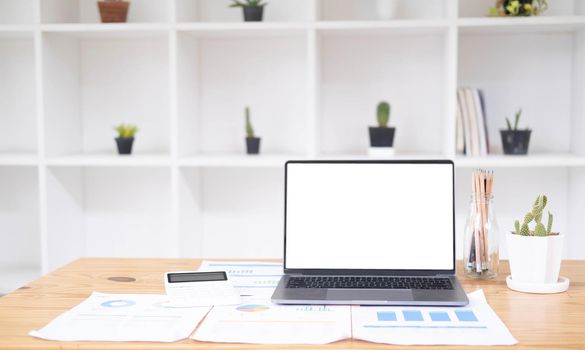 Close up of modern office desktop with blank white notebook screen, smartphone, coffee cup, supplies and other items. Mock up.