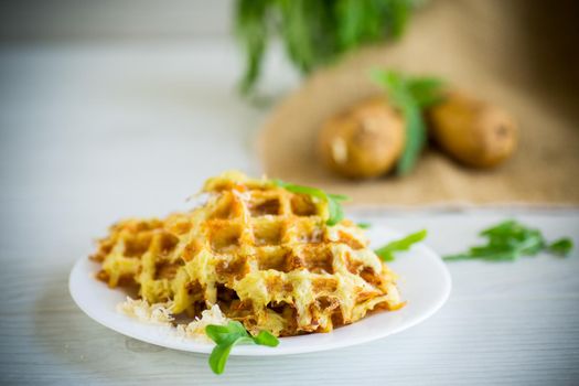 fried potato waffles with cheese in a plate on a light wooden table.