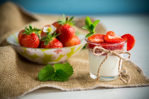 sweet homemade yogurt with strawberry jam and fresh strawberries in a glass cup, on a wooden table.