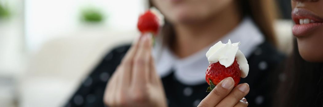 Close-up of afro american young woman hold strawberry with whipped cream. Best friends spend pastime together eating fresh berry at home. Bff, fun concept