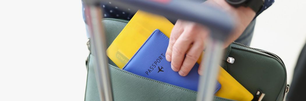 Close-up of man taking out flight documents of bag. Male hand holding passport and tickets. Boarding plane and departure lounge in airport. Travelling abroad concept