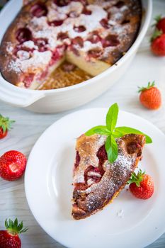 Sweet cottage cheese casserole with strawberry filling, in a plate on a wooden table.