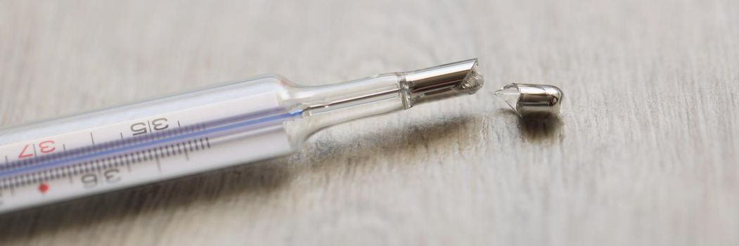 Close-up of broken glass mercury thermometer lying on floor. Crashed medical equipment. Mercury poisoning and life threatening idea. Healthcare and precautionary measures