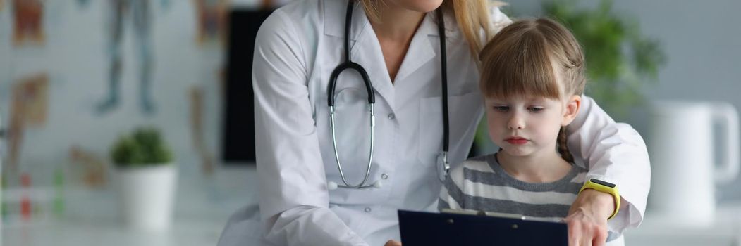 Portrait of mother doctor show to daughter medical history of patient. Mum entertain kid at work, teach new things and spend time. Family, clinic concept