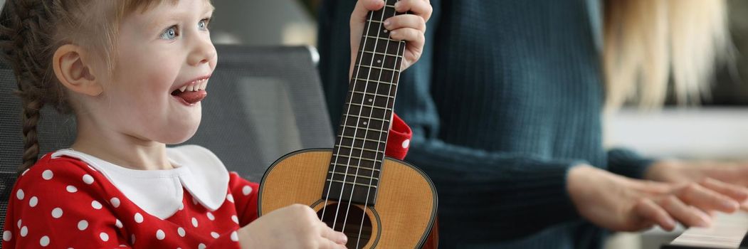 Portrait of happy child playing guitar and mother playing piano performing concert at home. Parent and daughter form home band. Music, creativity concept