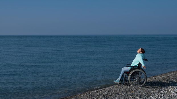 Caucasian woman in a wheelchair spread her arms like wings on the seashore