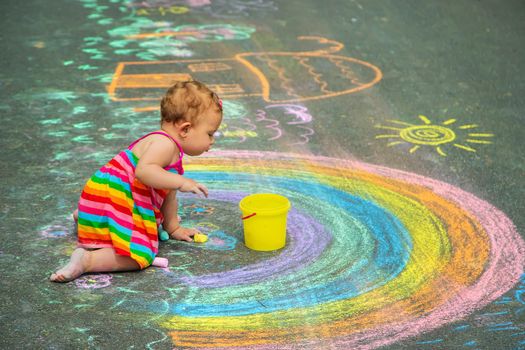 The child draws with chalk on the asphalt. Selective focus. Kid.
