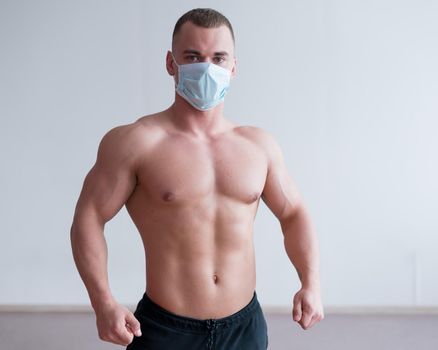 Male bodybuilder in a medical mask with muscular bare chest. The guy goes in for sports in quarantine. Respiratory protection