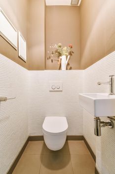 Modern toilet installed on beige wall under button and illuminated shelf in light restroom at home