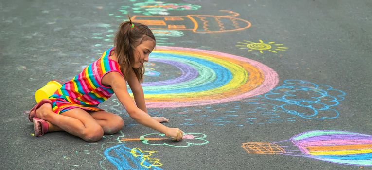 The child draws with chalk on the asphalt. Selective focus. Kid.