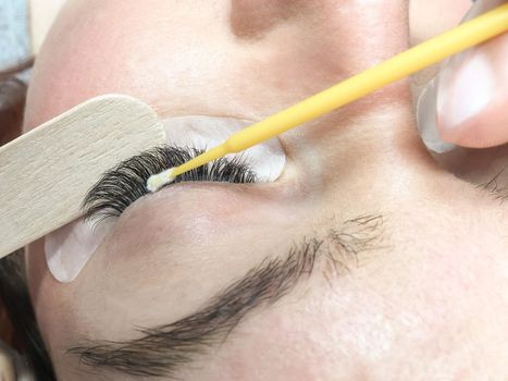 Close-up. The process of removing extended eyelashes. The master applies a creamy eyelash remover using a micro brush and a spatula. Cropped