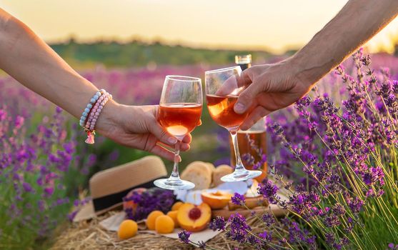 Wine in glasses is held by a woman and a man in a lavender field. Selective focus. Nature.