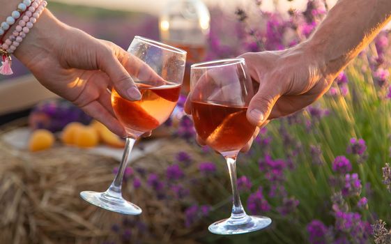 Wine in glasses is held by a woman and a man in a lavender field. Selective focus. Nature.