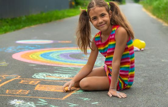 The child draws with chalk on the asphalt. Selective focus. Kid.