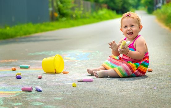 The child draws with chalk on the asphalt. Selective focus. Kid.