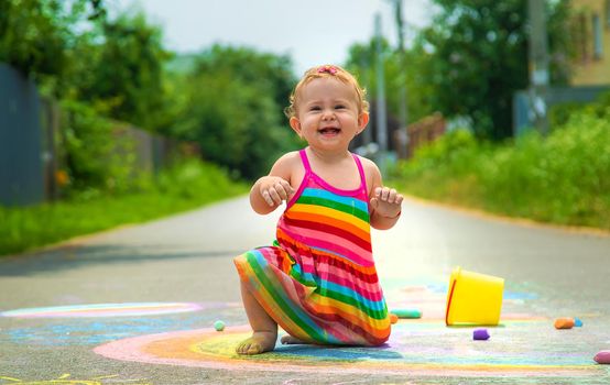 The child draws with chalk on the asphalt. Selective focus. Kid.