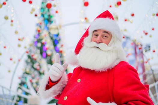 Portrait of an elderly man dressed as santa claus on the background of a christmas tree outdoors