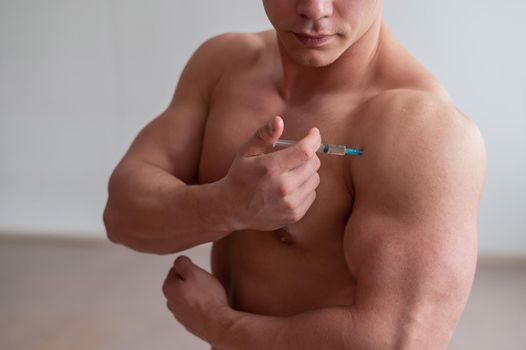 A muscular man with a naked torso holds a dope syringe. Unrecognizable bodybuilder puts himself steroids. Athlete cheats for gaining muscle mass