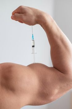 Closeup of a male hand with a dope syringe. Cropped biceps of a man. Unrecognizable bodybuilder sets himself growth hormone testosterone. Vertical photo