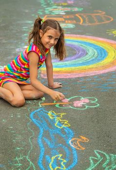 The child draws with chalk on the asphalt. Selective focus. Kid.