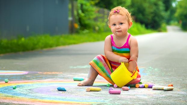 The child draws with chalk on the asphalt. Selective focus. Kid.