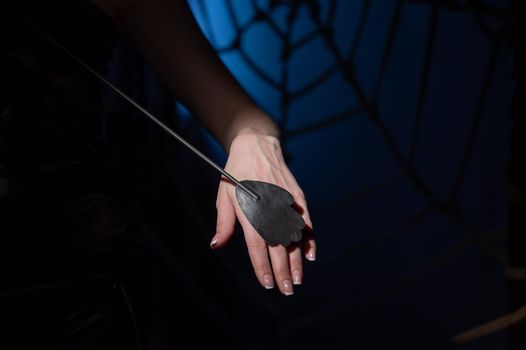 An unrecognizable woman demonstrates an elegant thin leather strip whip in a dark bedroom. Close-up of female hands with a bdsm toy. Pain and pleasure.Adult toy for slaps