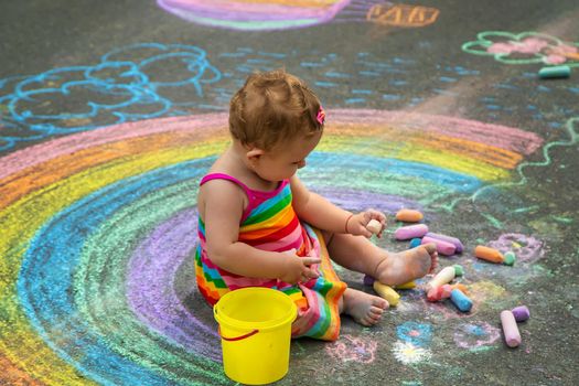The child draws with chalk on the asphalt. Selective focus. Kid.