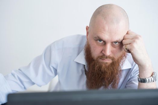 A focused bald man with a red beard stares intently at the camera. Male manager in a white shirt is angry at work