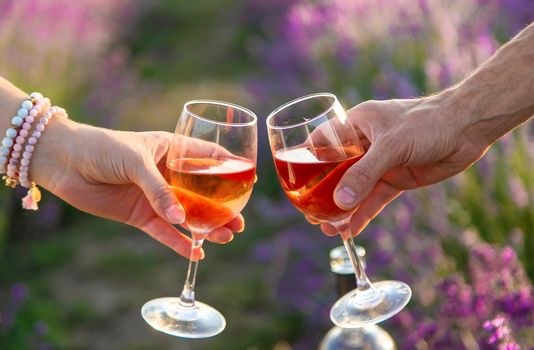 Wine in glasses is held by a woman and a man in a lavender field. Selective focus. Nature.