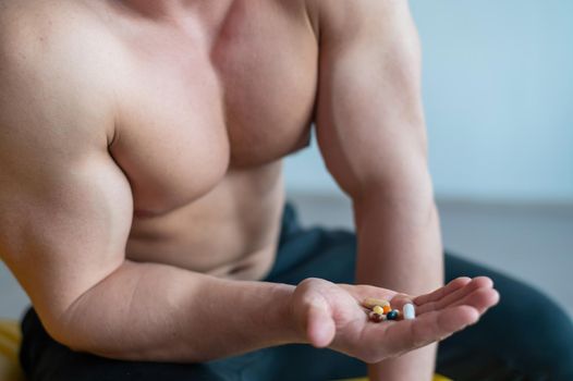 Faceless bodybuilder drinks capsules. A close-up of a muscular shirtless man holds a handful of vitamins and fitness supplements