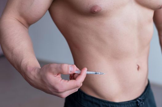 Close-up of a male torso. A shirtless bodybuilder puts a dope shot in his stomach. Faceless athlete puts an injection with illegal drugs