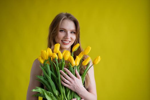 Caucasian woman with an armful of yellow tulips on a yellow background. International Women's Day. Bouquet of spring flowers.