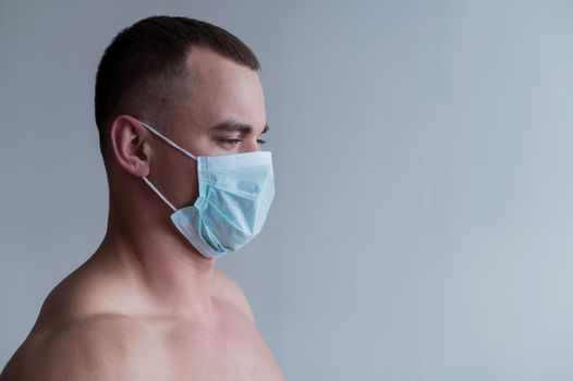 A male bodybuilder in a medical mask crossed his arms over his muscular bare chest. The guy goes in for sports in quarantine. Respiratory protection