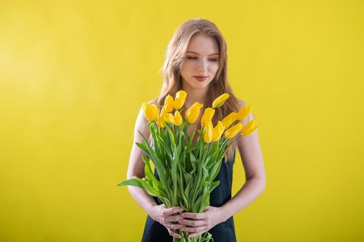 Caucasian woman with an armful of yellow tulips on a yellow background. International Women's Day. Bouquet of spring flowers.