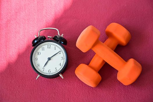 Two orange tunnels and an alarm clock on a pink yoga mat. Time to do fitness at home with equipment. Quarantine sports discipline.