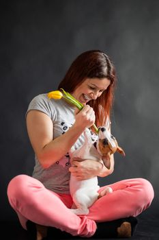 Red-haired woman holding a yellow tulip and playing with her puppy on a black background.