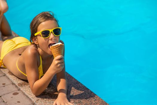 The child is eating ice cream near the pool. Selective focus. Kid.