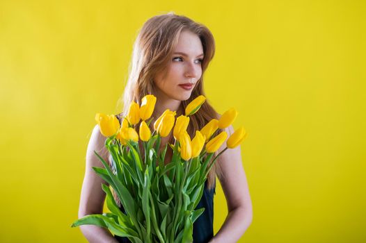 Caucasian woman with an armful of yellow tulips on a yellow background. International Women's Day. Bouquet of spring flowers.