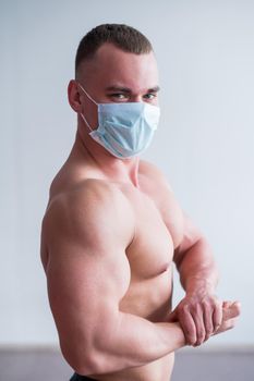 Bodybuilder with a naked torso in a medical mask. Muscular quarantine goes in for sports in quarantine. Respiratory protection
