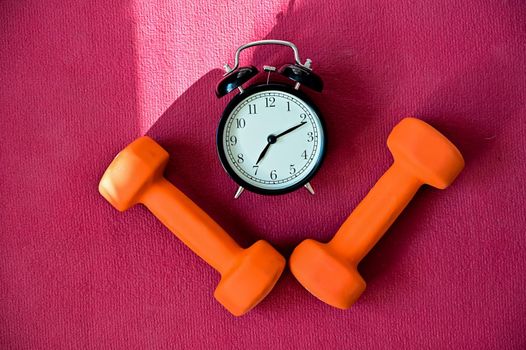 Two orange tunnels and an alarm clock on a pink yoga mat. Time to do fitness at home with equipment. Quarantine sports discipline.