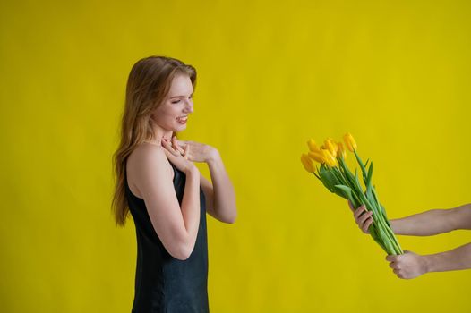 Caucasian woman accepts tulips as a gift on yellow background