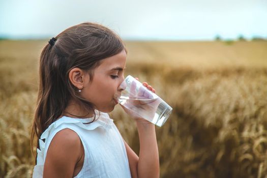 The child drinks water from a glass. Selective focus. Kid.