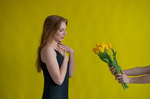 Caucasian woman accepts tulips as a gift on yellow background