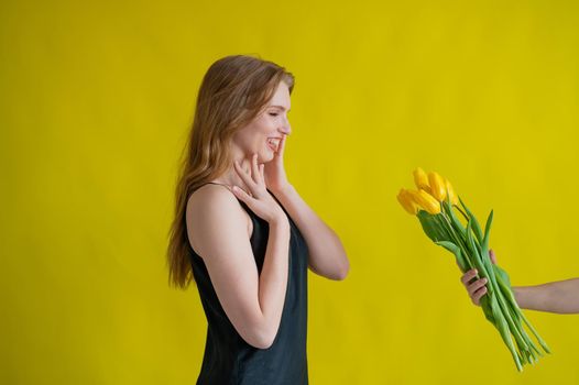 Caucasian woman accepts tulips as a gift on yellow background