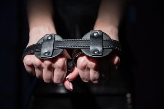 Close-up leather blindfolds in female hands. Unrecognizable woman holds bdsm equipment in the dark. Sexual role-playing games for adults. Humility and dominance